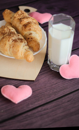 Romantic Valentines day breakfast - delicious fresh croissants with milk and pink felted hearts on purple background, copy spaceの写真素材