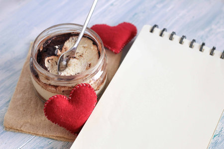 Homemade italian dessert tiramisu in jar with felted hearts and notebook, copy space place for textの写真素材