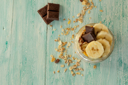healthy delicious dessert - muesli and yogurt with banana, nuts and chocolate on turquoise wooden backgroundの写真素材