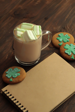 Decorative cookies, a mug with cocoa and notebook on tray Saint Patricks Day concept place for textの写真素材