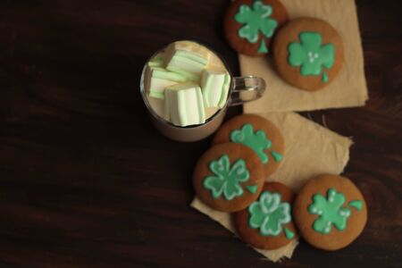 Homemade gingerbread Gourmet St Patrick Day cookies and a mug of coffee with marshmallows on dark wooden background St Patrick day celebration top view place for text.の写真素材