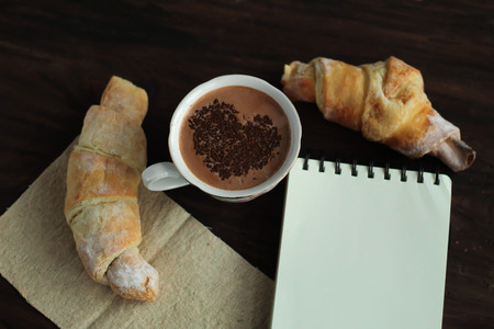 Romantic breakfast - delicious fresh croissants, cocoa with chocolate topping and sketchbook top view place for textの写真素材