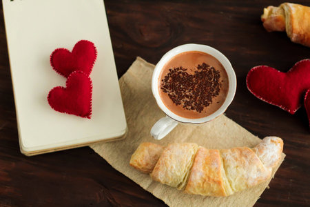 Cup of Hot Chocolate with heart shaped topping and croissants with chocolate, Empty Notebook for Notes romantic breakfast idea top viewの写真素材