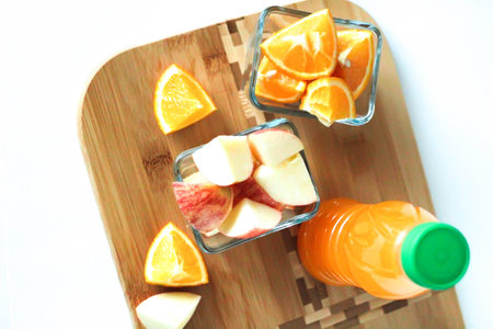Orange juice in the bottle, cut apples and oranges in glass bowls on wooden board Summer time concept top viewの写真素材