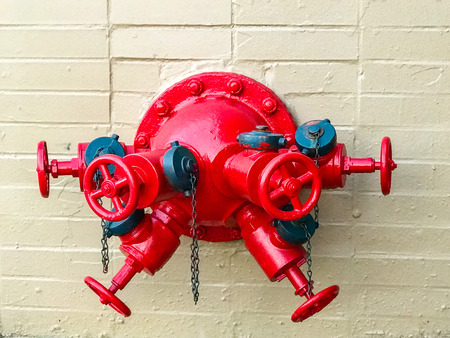 Red fire hydrant with multiple connections on a stone wallの写真素材