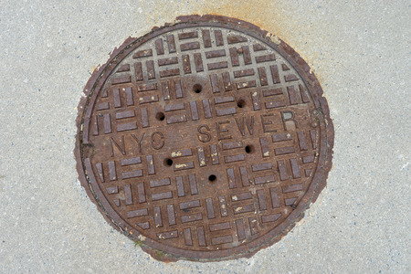 Old rusty sewer hatch on concrete surface, New York City.の写真素材