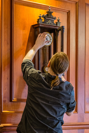 Watchmaker winding up vintage wooden pendulum clock hanging on a wallの写真素材