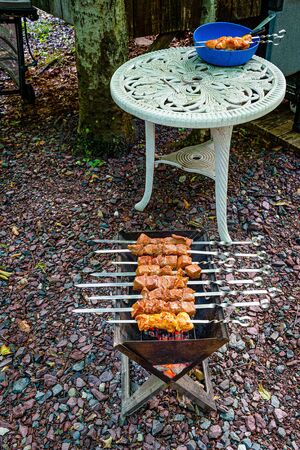 Pieces of raw marinated meat strung on skewers are cooking on a grill. Pieces of raw marinated meat strung on skewers in a blue bowl on a vintage white table.の写真素材
