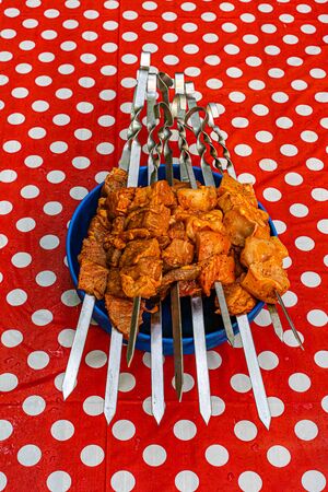 Pieces of raw marinated meat strung on skewers in a blue bowl on a red tablecloth with large white circles. Ready to cook.の写真素材