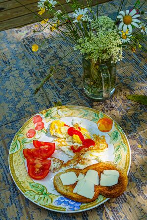 Full breakfast - fried eggs, ketchup, sliced tomato, toasted slice of white bread with slices of butter on a white plate with an ornament on a wooden table covered with a tablecloth, top view.の写真素材
