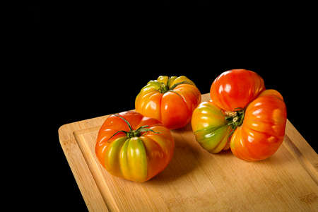 Three Big farm organic tomato on cutting board, black backgroundの写真素材