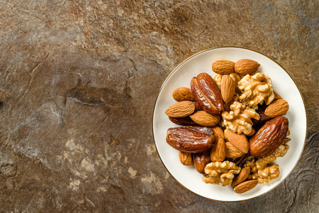 Raw almonds, organic pitted dates and walnut halves in white porcelain saucer with gold border on...