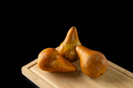 three brown pears on wooden cutting board isolated on black backgroundの写真素材