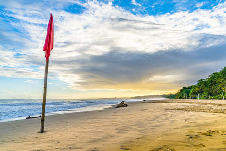 Sunrise at Playa Cocles, beautiful tropical Caribbean beach, Puerto Viejo, Costa Rica east coast and a wooden stick with a red flagの写真素材