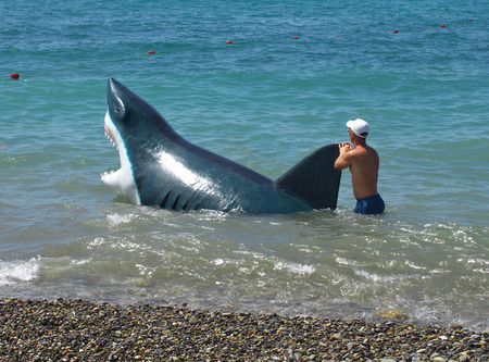 Sochi, Russia - June 30, 2014: Man walks with a hoax sharks in the water along the beach in Sochiのeditorial素材
