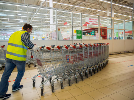 Voronezh, Russia - Juny 13, 2020: A worker collects empty carts at the Auchan supermarket, Voronezh