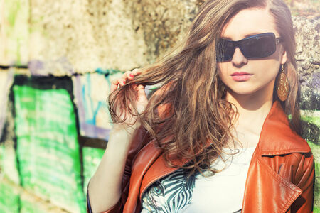 young beautiful girl in the solar points stands near the wall with graffiti in the cityの写真素材
