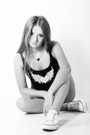 beautiful young girl in jeans shorts and a sports Shoe sitting in the Studio on the white-blue backgroundの写真素材