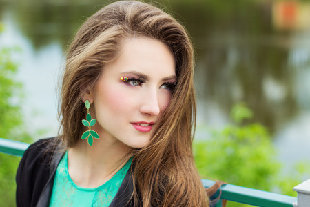 young beautiful sexy girl in a green dress with beautiful makeup with green shackles sitting on the river Bank in the cityの写真素材