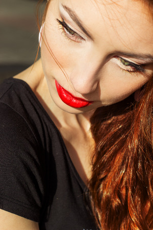 beautiful sexy girl with red hair with big red lips with makeup in the city on a Sunny summer dayの写真素材