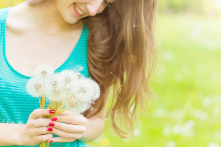 beautiful happy smiling girl with long dandelions in the hands of shorts and a t-shirt is resting in the Park on a Sunny dayの写真素材