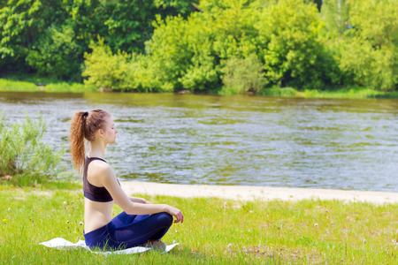 beautiful young girl is engaged in sports, yoga, fitness on the beach by the river on a Sunny summer dayの写真素材