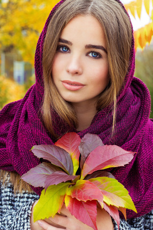 beautiful charming young attractive girl with large blue eyes with a handkerchief on his head, long dark hair holding a fall bouquet of leaves on a cold autumn dayの写真素材