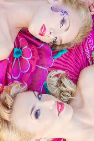 beautiful sexy girls, sisters with bright makeup and red lips lie on a bright blanket in a Park on a warm summer dayの写真素材