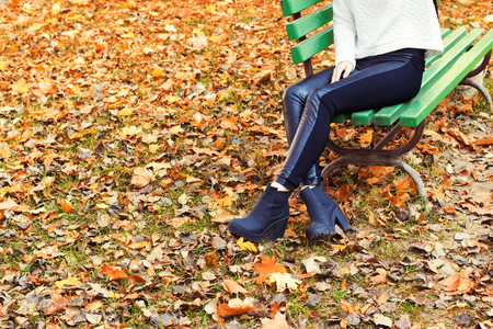 beautiful legs girl in black pants and boots sitting on the bench in autumn Parkの写真素材