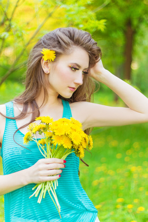 beautiful girl in a Sunny summer day walking in the garden and keeps yellow dandelions in the handsの写真素材