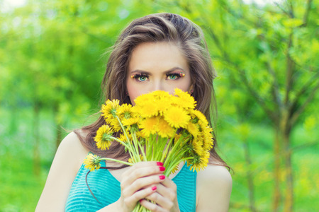 beautiful girl in a Sunny summer day walking in the garden and keeps yellow dandelions in the handsの写真素材