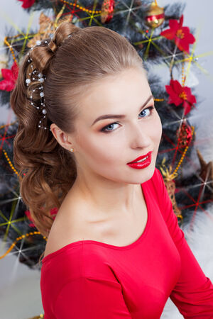 beautiful sexy happy smiling young woman in evening dress with bright makeup with red lipstick sitting near the Christmas tree in a festive Christmas eveningの写真素材