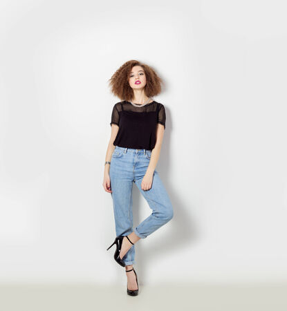 beautiful sexy girl in jeans and a black t-shirt standing near a white wall, bright makeup and hairstyle, photo in Studioの写真素材