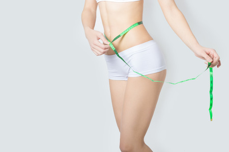 young sports a beautiful slim woman measuring perfect shape nice hips, the concept of a healthy lifestyle on a white backgroundの写真素材