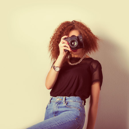 beautiful young sexy woman in jeans with a camera in the hands of curly hair in the Studio, retro...