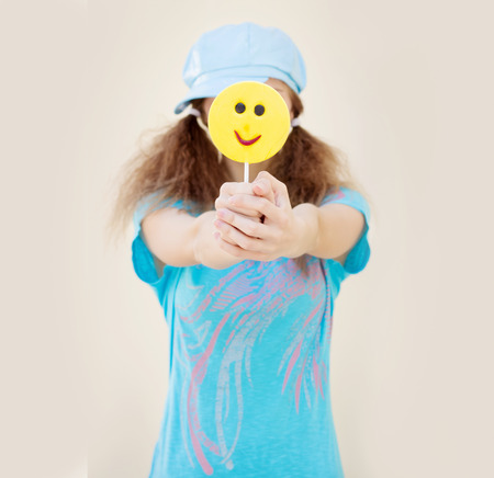 girl in blue shirt and cap with two tails holds in front of a big yellow candyの写真素材