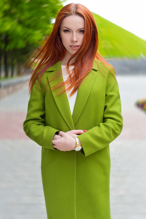 beautiful sexy woman with fiery red hair with green coat walking through the streets of the cityの写真素材