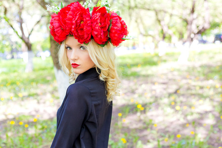Portrait of beautiful sexy blonde girl with a wreath of peony walks in the garden on a sunny dayの写真素材