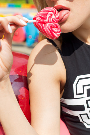 beautiful sexy girl tenderly licking bright colored candy on a stick in the form of heartの写真素材