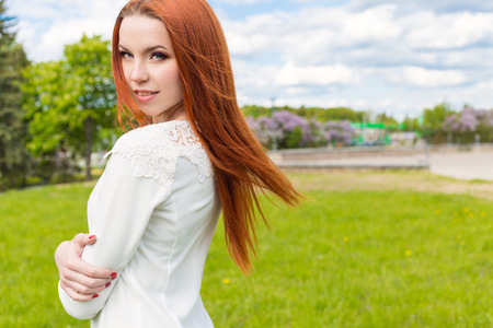 Happy beautiful sexy redhaired girl in a white dress walks in the parkの写真素材