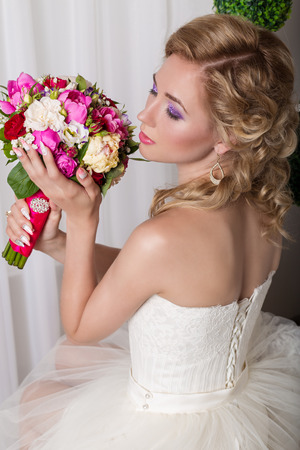 beautiful gentle young girl happy bride in a white dress sitting on a chair and smelling a bridal bouquet with a nice manicureの写真素材