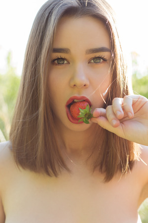beautiful sexy cheerful woman with full lips sexy eating strawberries in the street at sunset on a sunny summer dayの写真素材