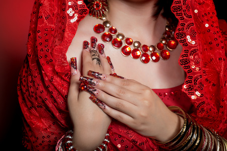 beautiful girl in the image of Indian woman in a red sari with beautiful patch acrylic nails in oriental style in the studioの写真素材