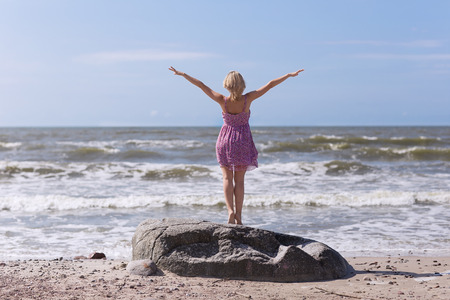 Young beautiful slim girl standing on the beach on a sunny summer day, a strong wind on the seaの写真素材