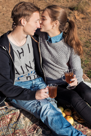 beautiful young happy couple in love sitting on lake shore on a warm Sunny evening kissing and drinking warm teaの写真素材