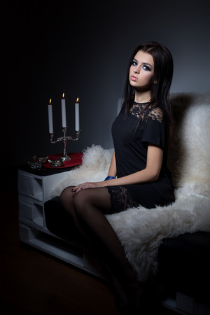 beautiful sexy sweet girl with full lips bright makeup sitting on the sofa with a glass of wine in a black evening dressの写真素材