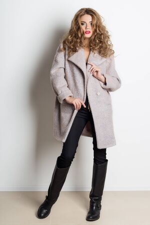 beautiful sexy girl with bright makeup posing in the coat in the studio on a white background, shot for the catalogの写真素材