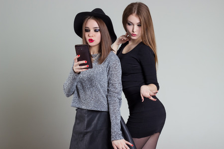 Two cheerful smiling sexy girl girlfriends photographed on the phone, do selfie phone in the studio on a gray backgroundの写真素材