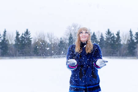 beautiful cute sexy playful happy young woman in a blue coat in the cap playing with snow in the parkの写真素材