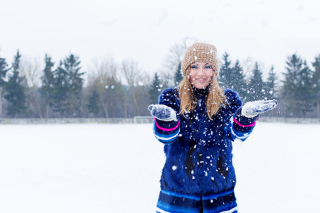 beautiful cute sexy playful happy young woman in a blue coat in the cap playing with snow in the parkの写真素材